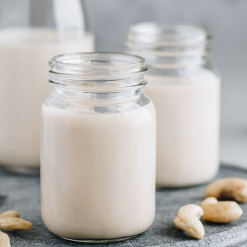 A couple of nice glass jars filled with white nut milk sitting on a nice counter.