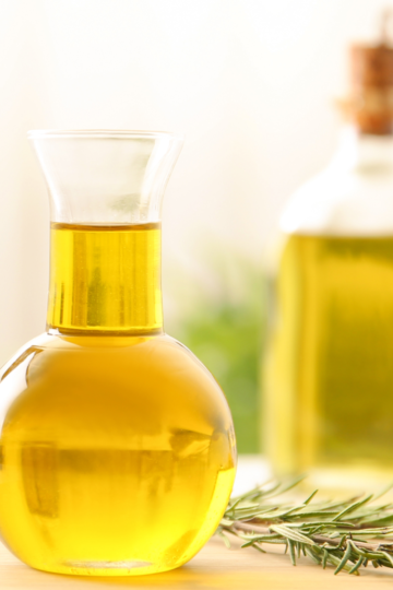 A nice glass pouring vessel holding oil used for baking, resting on a wooden countertop.