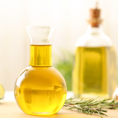 A nice glass pouring vessel holding oil used for baking, resting on a wooden countertop.