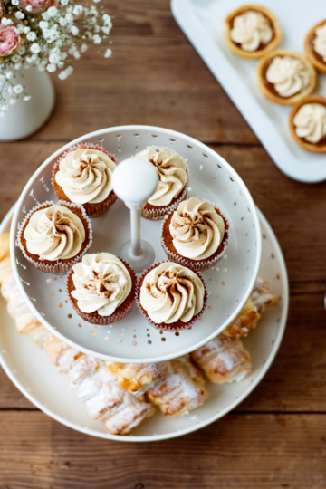A nice wooden party table set with fancy cupcake stands filled with bakery style cupcakes.