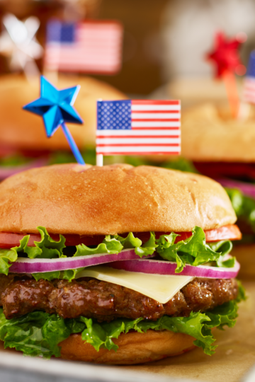 Perfect hamburgers with all the toppings resting on a table with patriotic toppers.