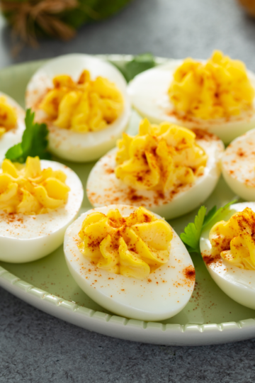 Beautiful deviled eggs topped with paprika served on a ceramic egg shaped plate.