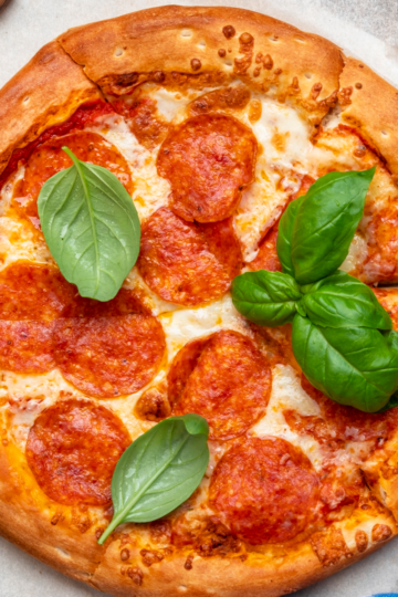 A large pepperoni pizza resting on a countertop ready to be served to a large group.