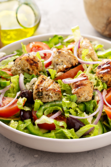 Large bowl of fresh green salad for a crowd with chicken, onions, olives and tomatoes.