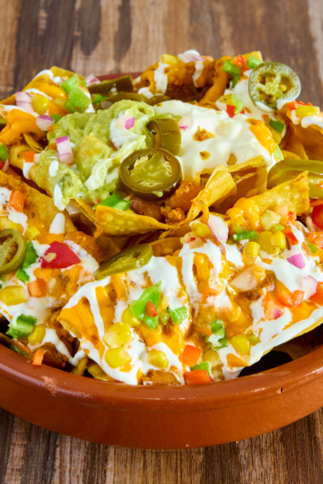 A bowl filled with colorful nachos topped with sour cream, cheese, jalapeños and corn.