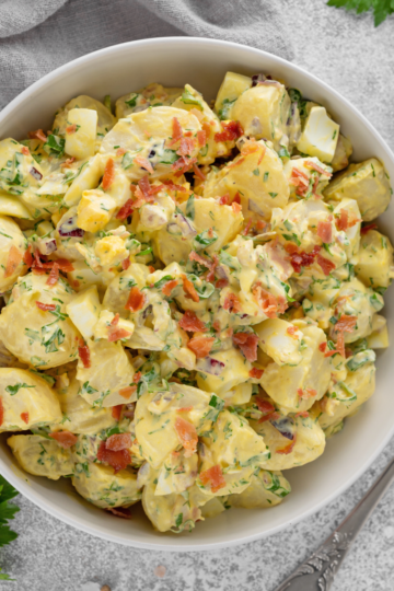 A white bowl brimming with fresh colorful potato salad, perfectly dished and ready to serve a crowd.