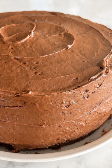 Rich and chocolatey sourdough discard cake resting on a ceramic plate frosted with decadent chocolate buttercream.