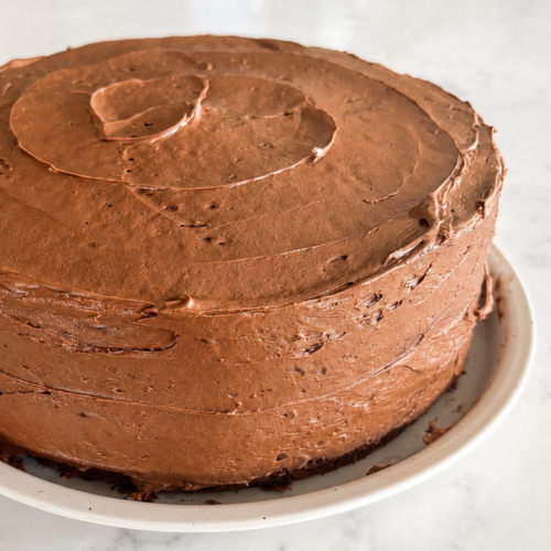 Rich and chocolatey sourdough discard cake resting on a ceramic plate frosted with decadent chocolate buttercream.
