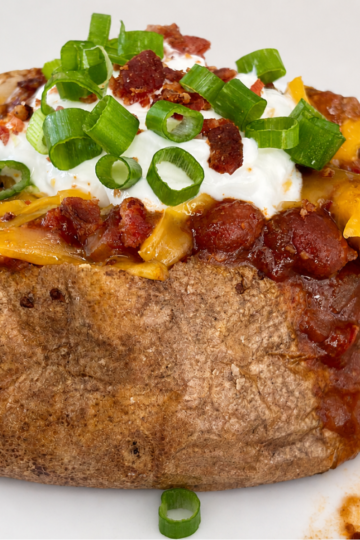 Baked potato bar for a crowd with loaded potatoe and toppings including sour cream, shredded cheese, bacon, chili, and green onion.