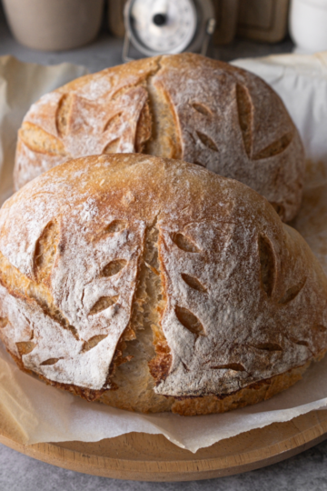 Multiple golden-brown sourdough loaves on a wooden counter with a kitchen scale and banneton, scaled from a single recipe.