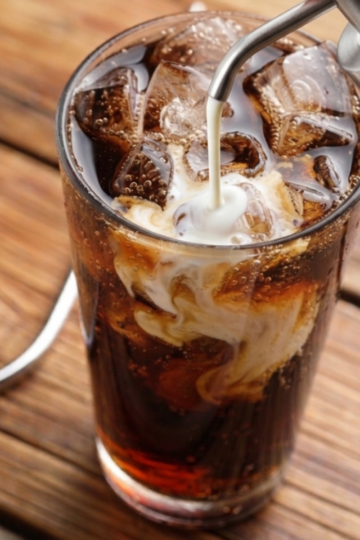 Cream being poured over ice into a tall glass of cola to make a dirty soda