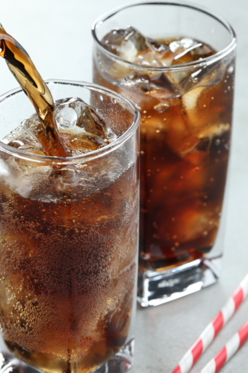 Two tall glasses of cola over ice on a marble counter top.
