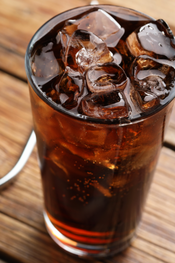 Tall glass of cola over ice on a wooden table