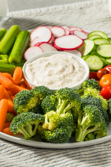 Veggie tray with baby carrots, celery, radishes, cucumber, broccoli, and cherry tomatoes around a bowl of creamy ranch dip.