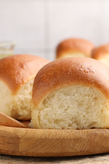 Soft dinner rolls with golden tops and pull-apart sides on a round wooden board lined with parchment paper