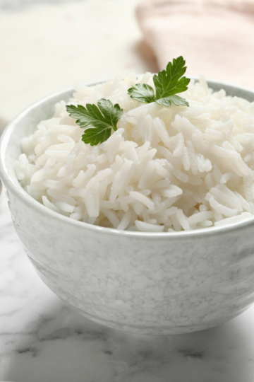 Bowl of fluffy cooked long-grain white rice garnished with fresh parsley, with a serving spoon on a marble counter