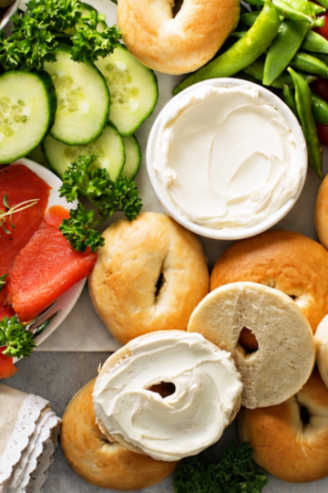 Bagel bar spread for a crowd with plain bagels, cream cheese, smoked salmon, cucumber, and cherry tomatoes.