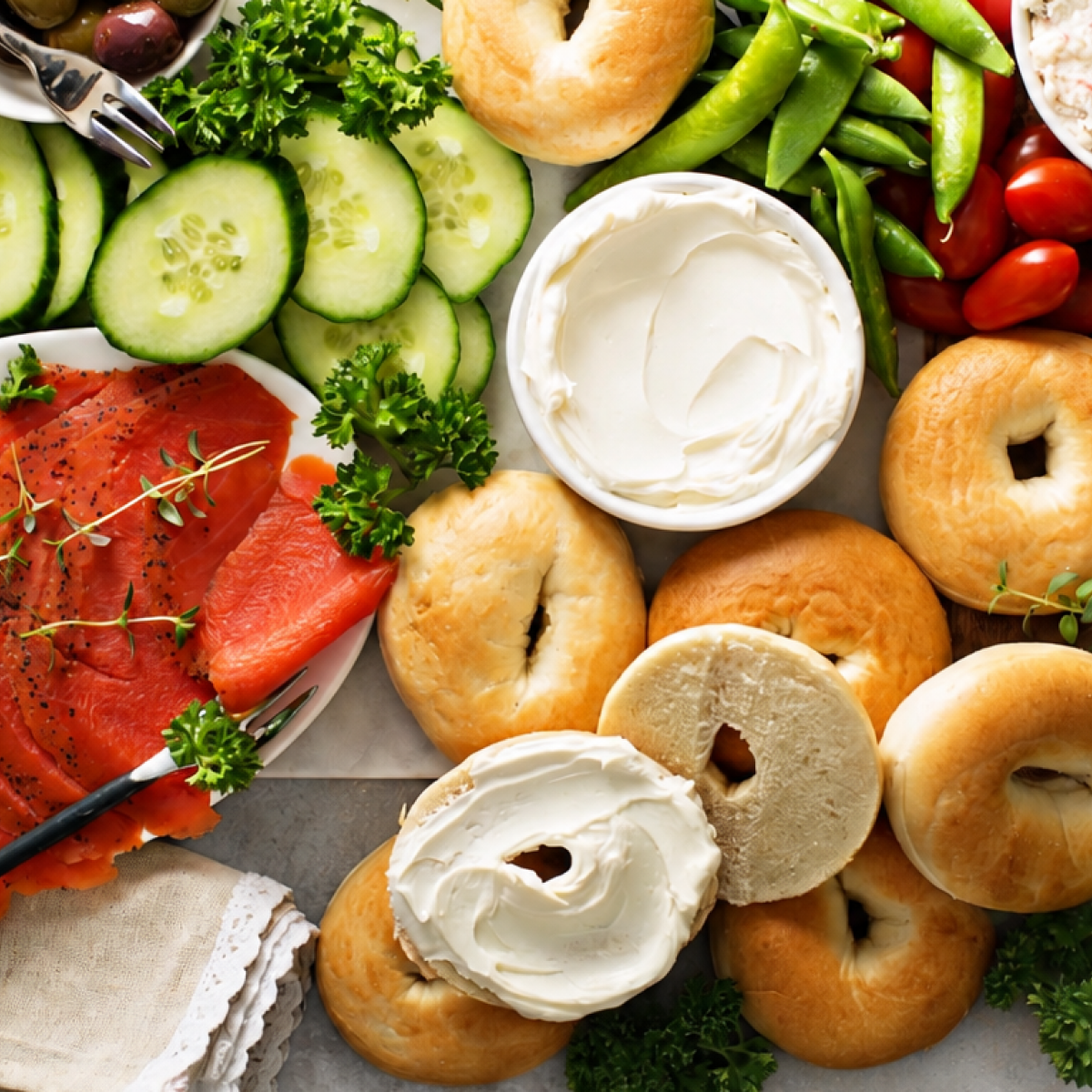 Bagel bar spread for a crowd with plain bagels, cream cheese, smoked salmon, cucumber, and cherry tomatoes.