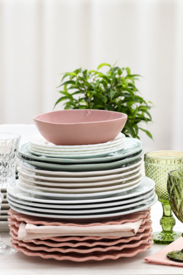 Stacked dinner plates, salad plates, and scalloped pink chargers with green goblets and crystal stemware set out for a party