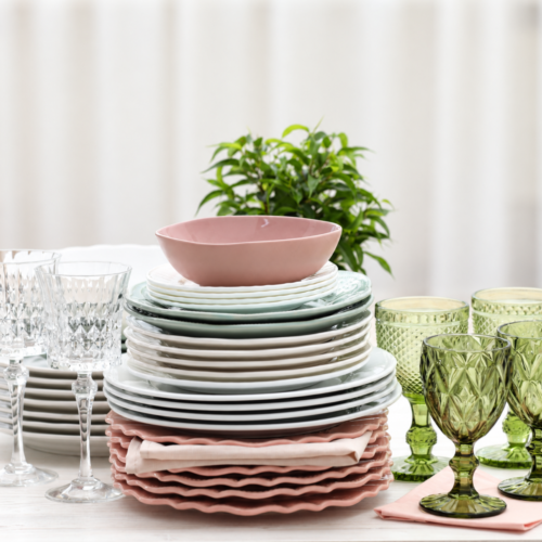 Stacked dinner plates, salad plates, and scalloped pink chargers with green goblets and crystal stemware set out for a party