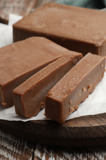 Thick slab of chocolate fudge with three strips cut from it, on parchment paper over a round wooden board.