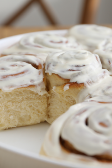 Frosted homemade cinnamon rolls in a white round baking dish, with one roll pulled away to show the soft, fluffy inside